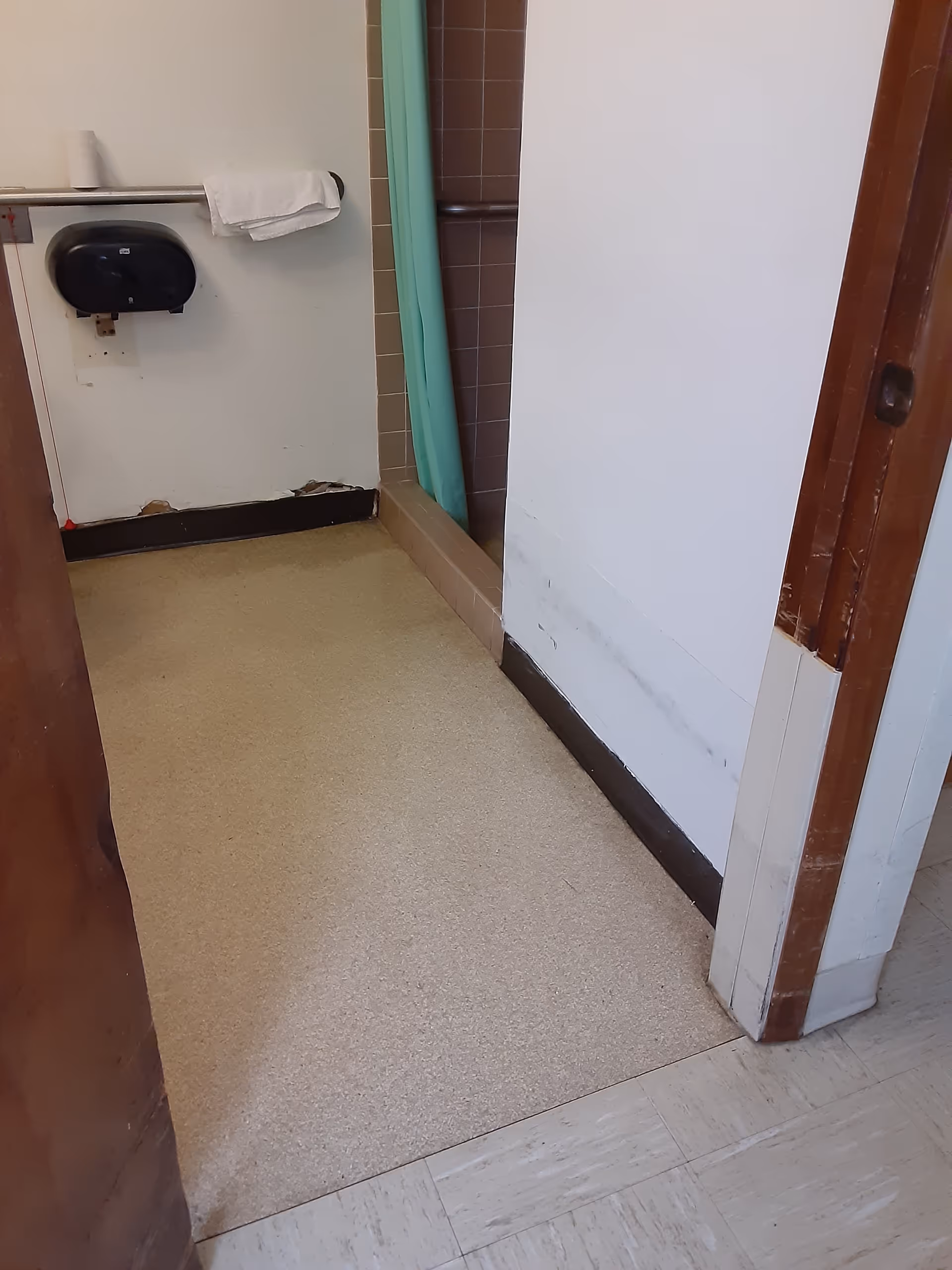 Narrow bathroom area with sink, paper towel dispenser, towel rack, and shower curtain.