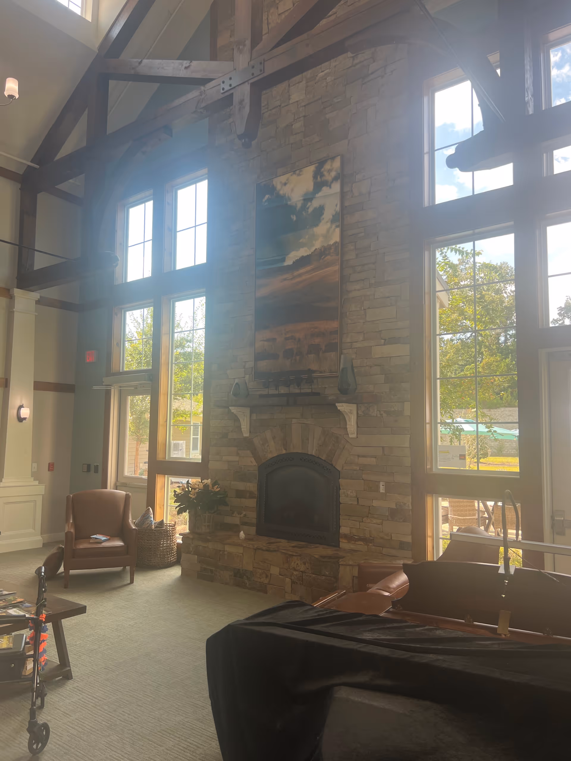 Tall stone fireplace with large windows and wooden beams in a spacious senior living lounge.