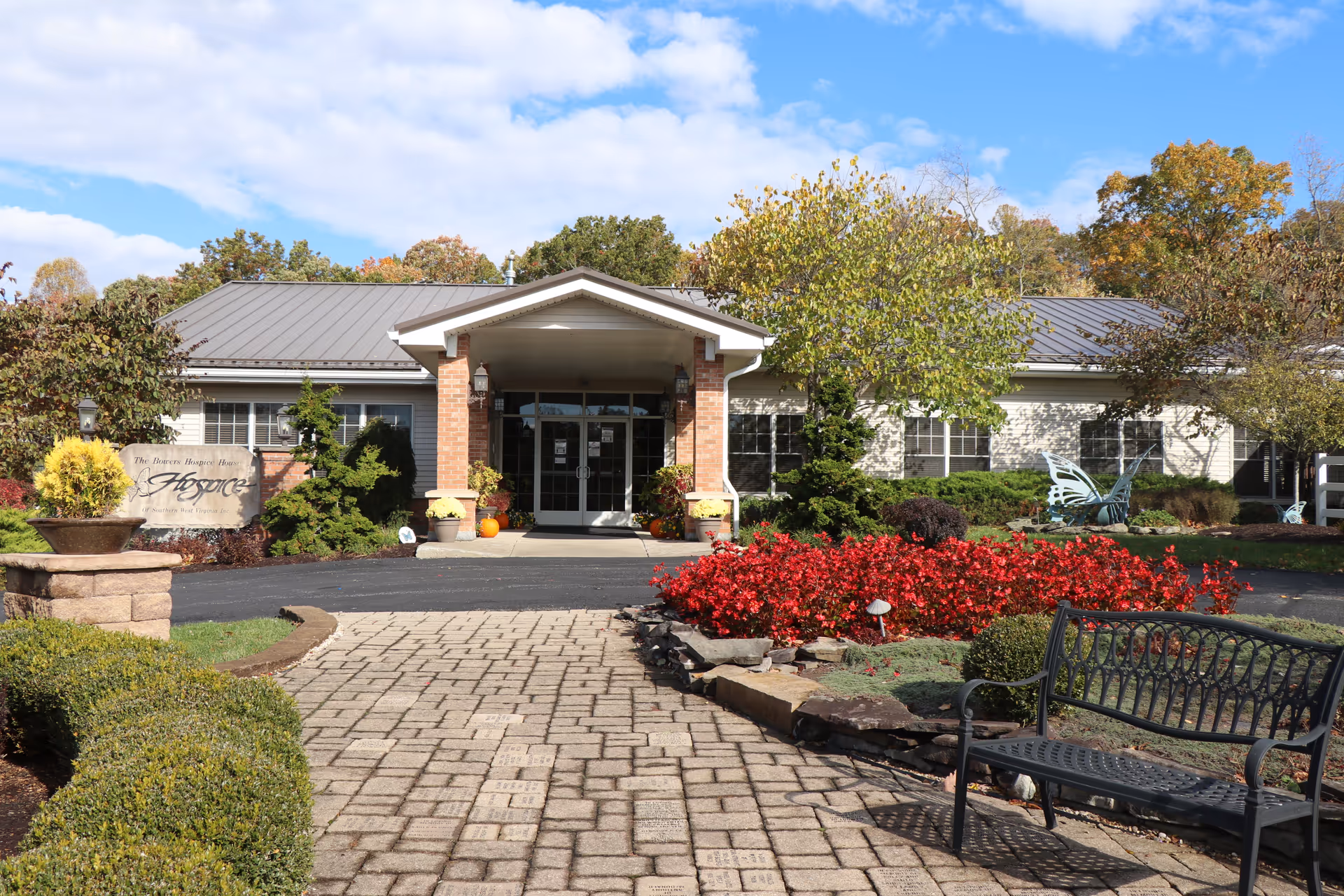 Exterior view of a hospice facility entrance with brick columns, landscaped garden, and a bench.