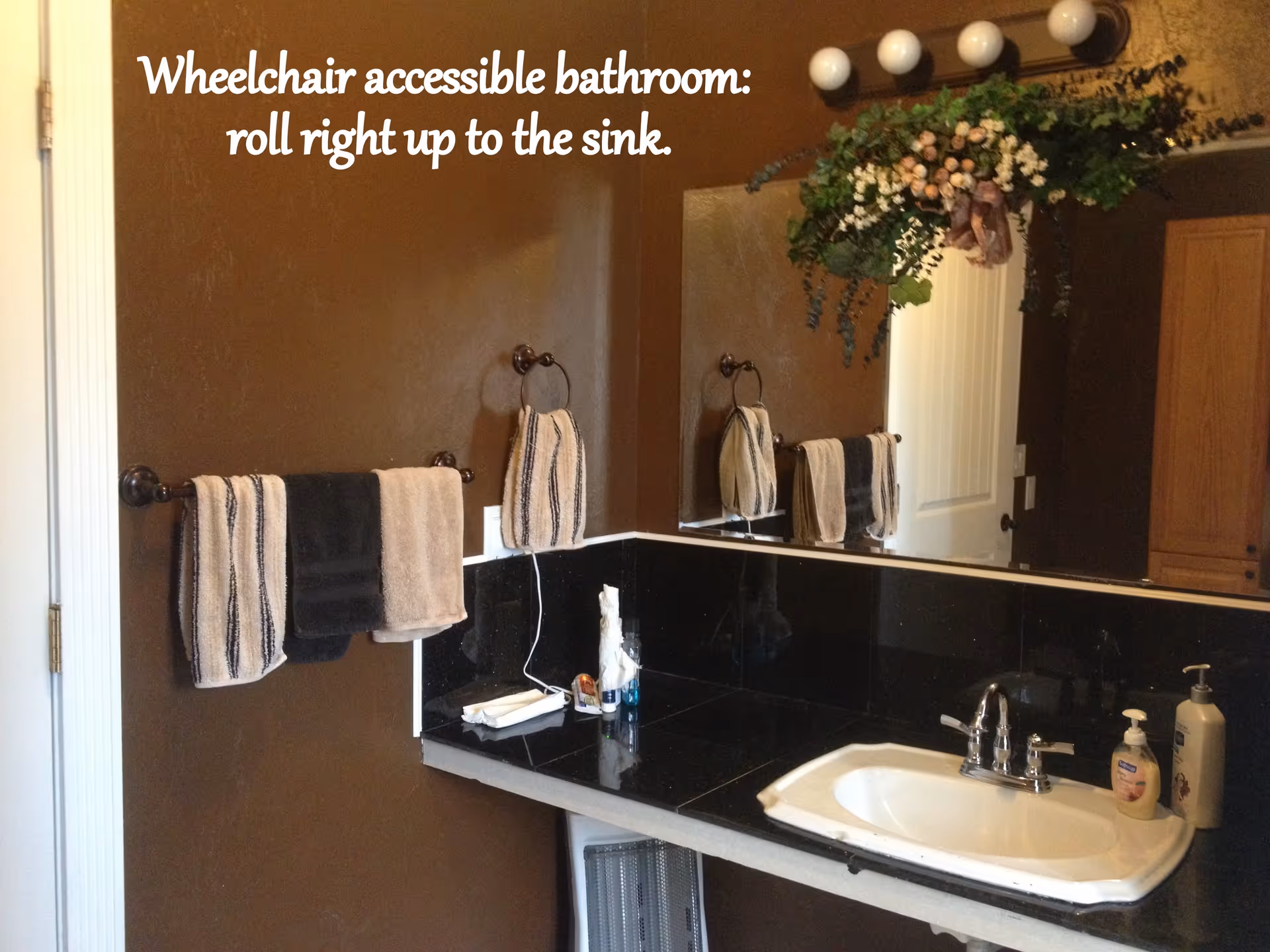 Bathroom sink and countertop with large mirror, hanging towels, soap dispensers and decorative greenery above.