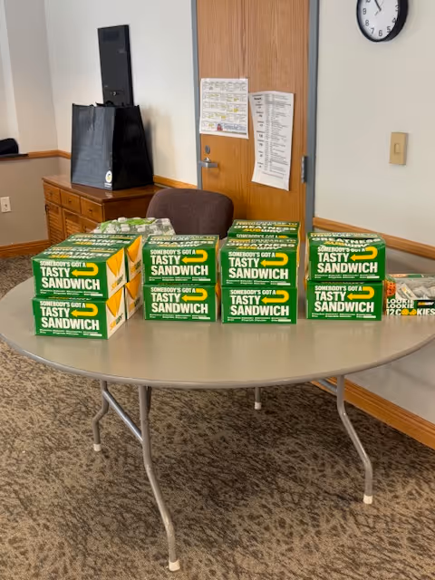 Round table with several green sandwich boxes in a senior living facility lounge.