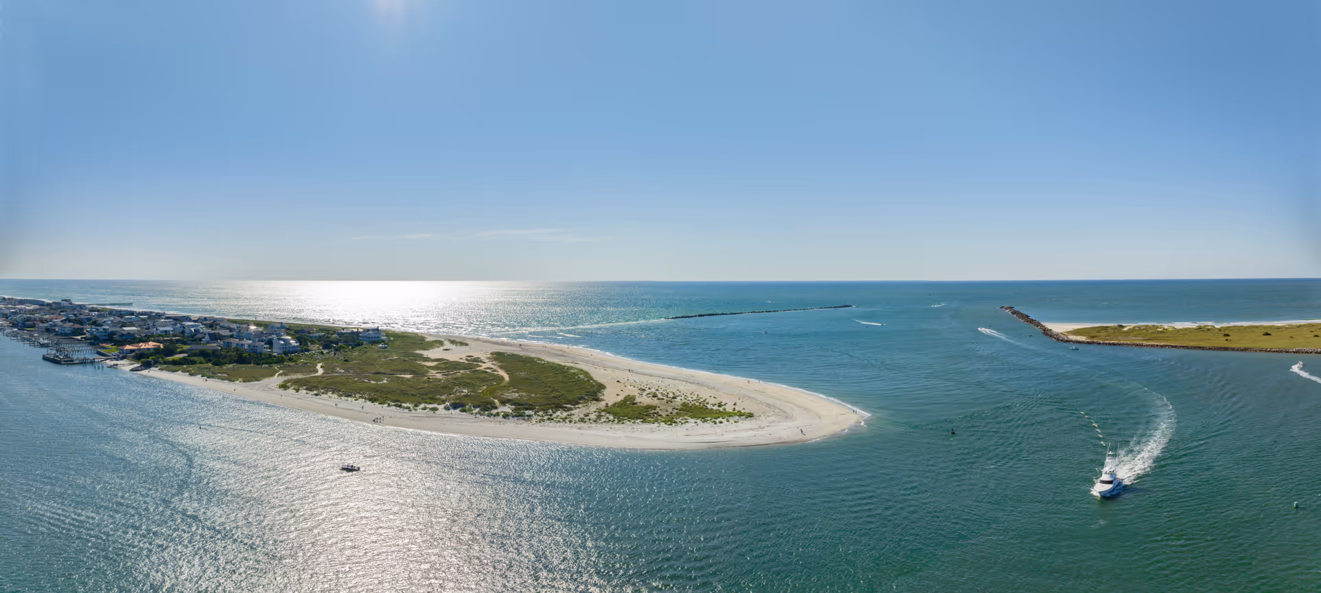 Aerial view of a coastal landscape with a sandy island and a speedboat.