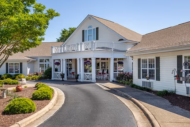 White senior living facility exterior with a curved driveway and welcoming front porch