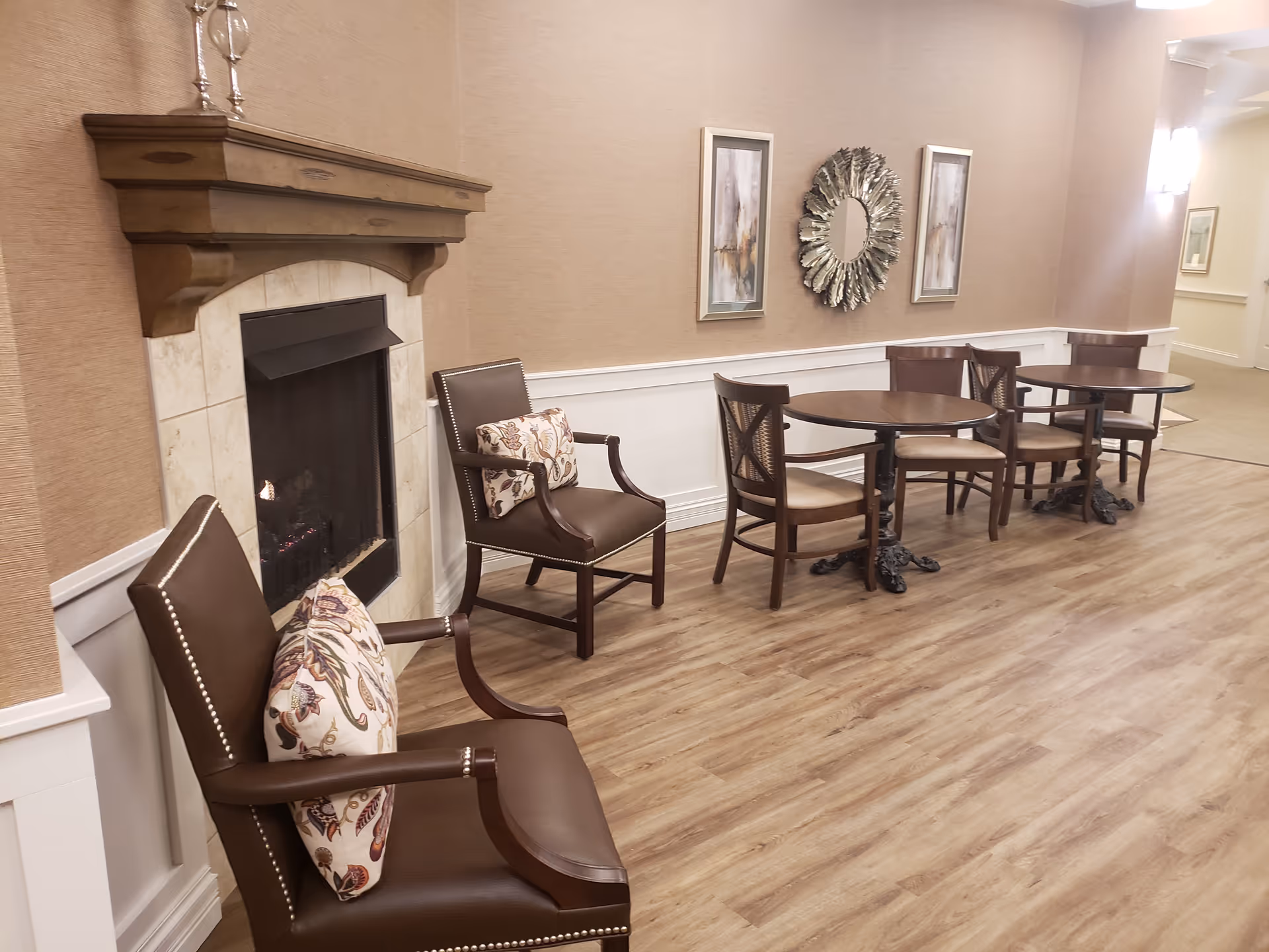 Interior of a senior living lounge with a fireplace, chairs, and round tables.