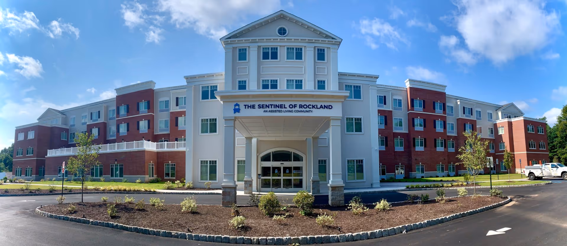 Front view of a large senior living building with a covered entrance and landscaped circular drive.