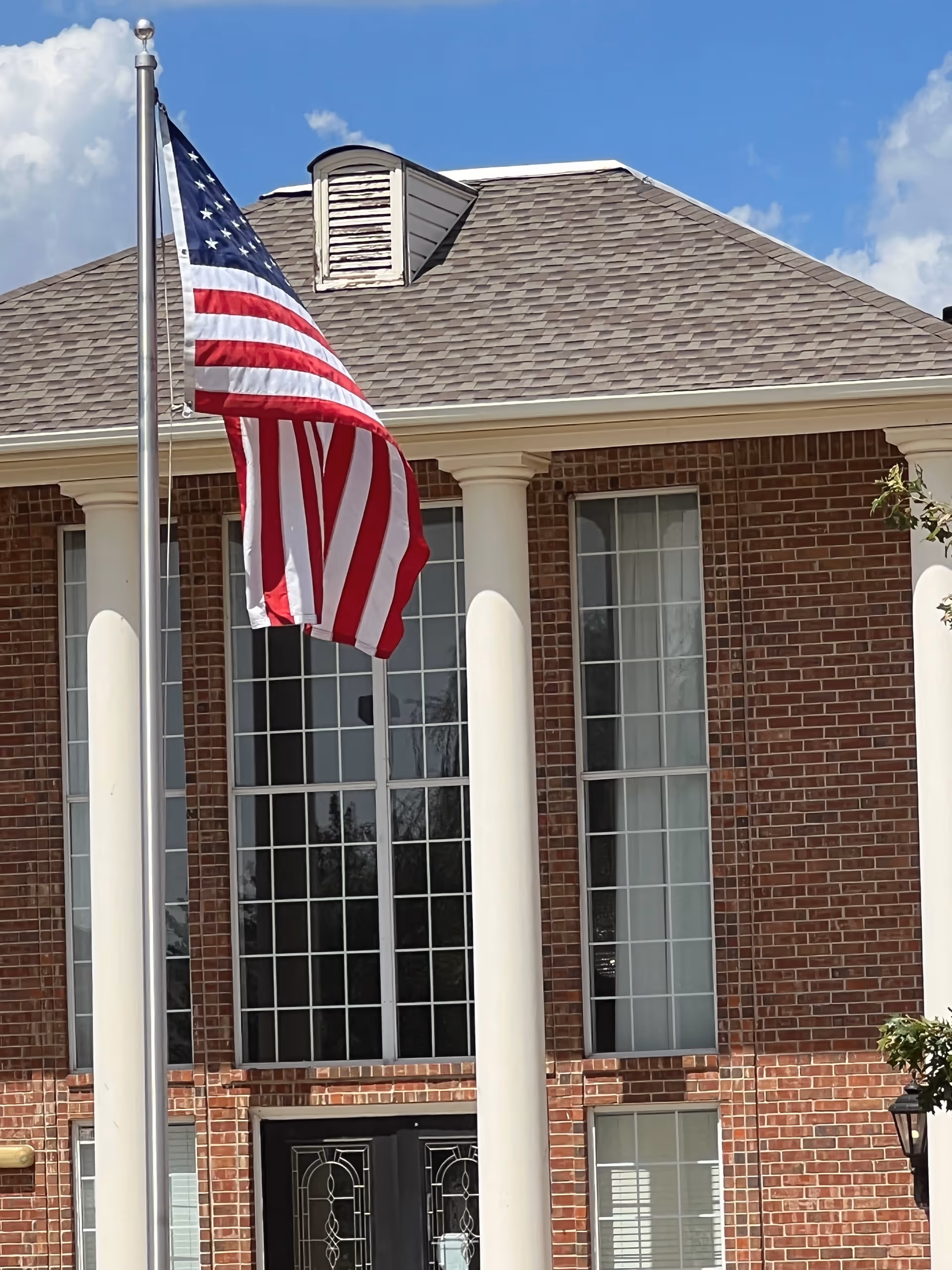 Front of brick senior living facility with flag, white columns, and tall windows.