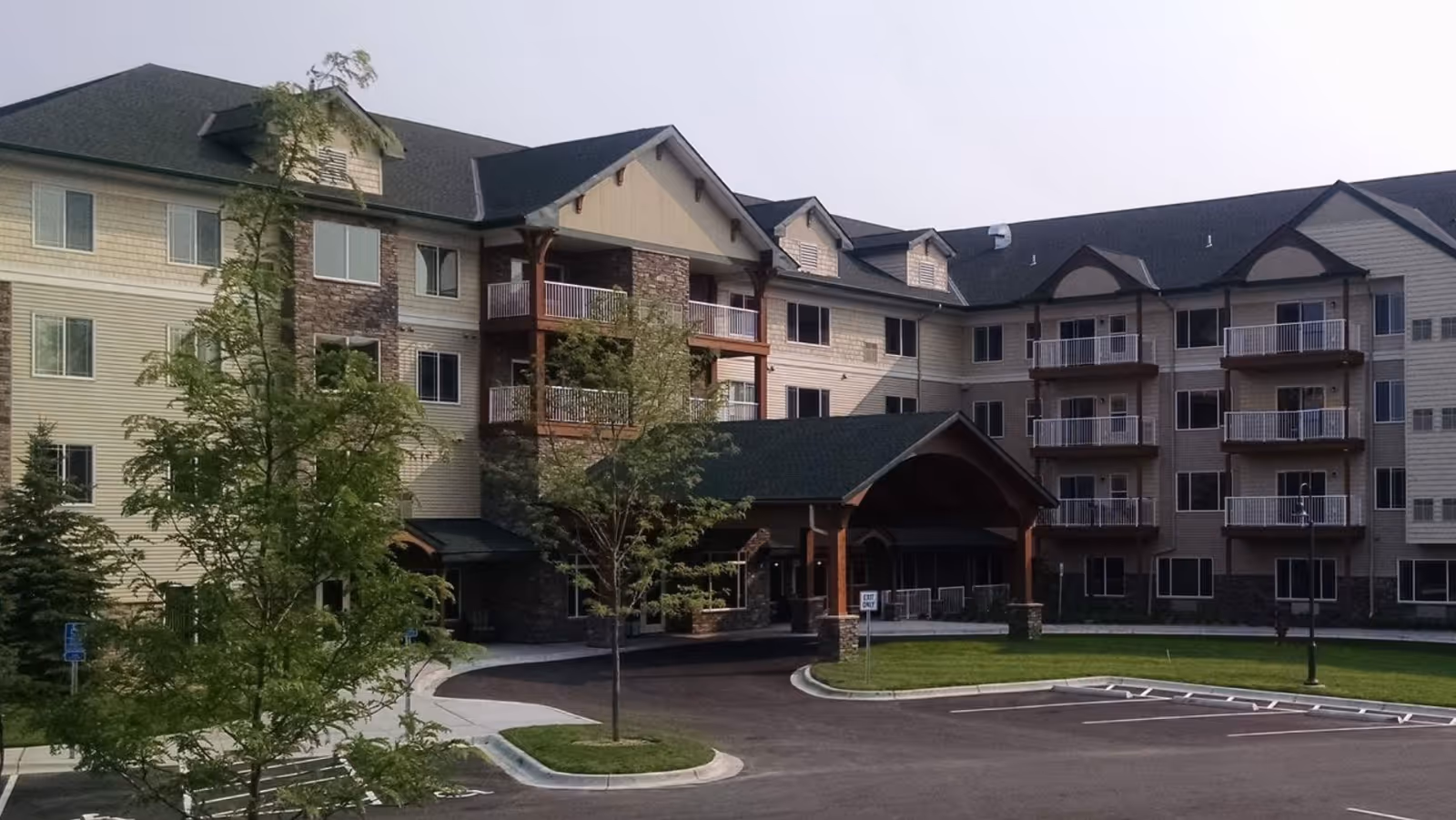Three-story beige senior living building with a covered entrance and parking.