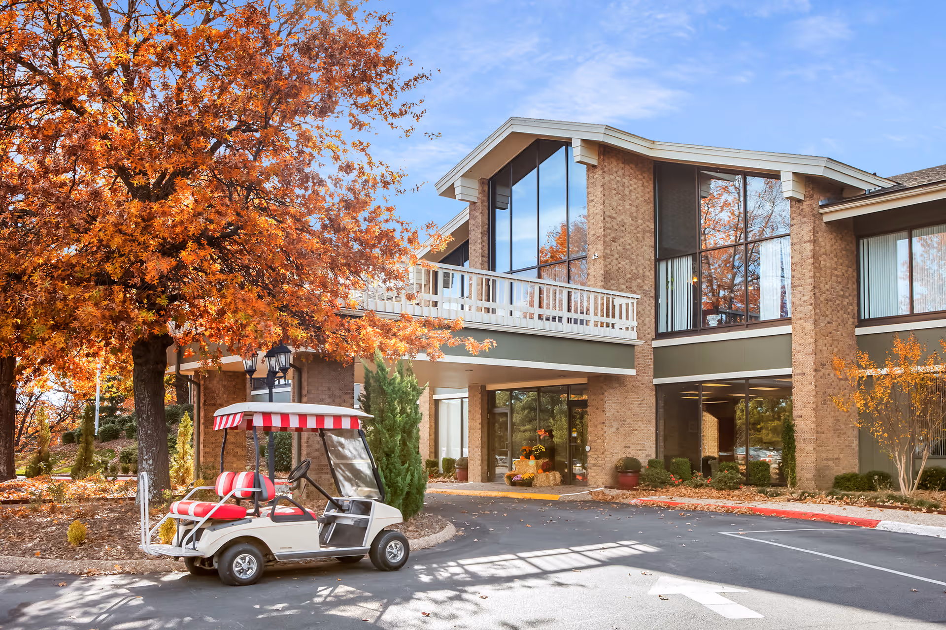 Exterior view of Concordia of Bella Vista with autumn tree, front entrance, and a golf cart.