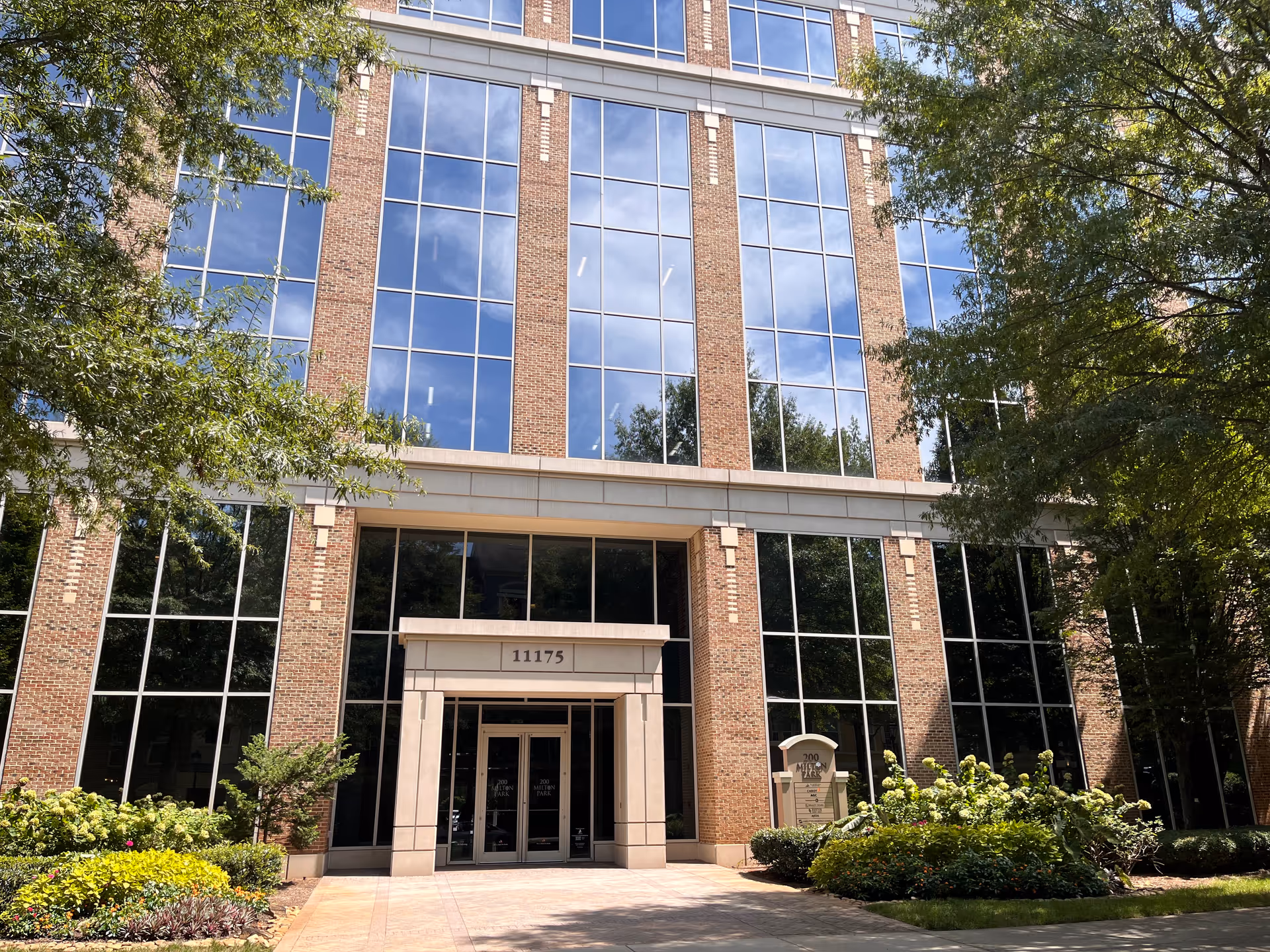 Brick-and-glass office building facade with wide glass windows, central entrance, and landscaping.