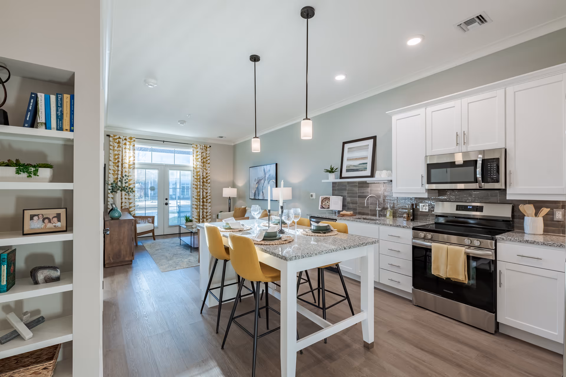 Open-concept kitchen and living area with a central island, yellow bar stools, stainless steel appliances, and a seating area by glass doors.