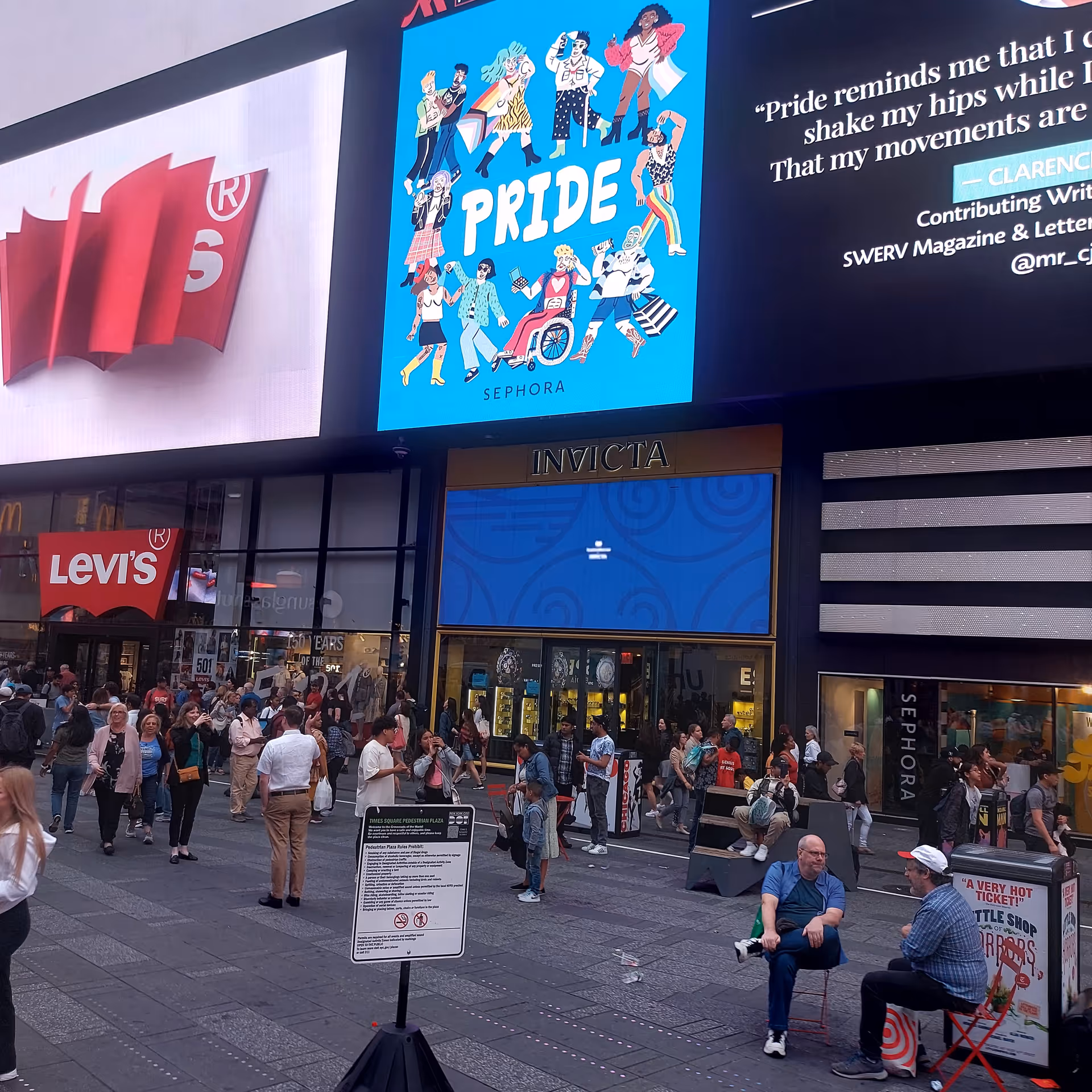 Busy city street with large digital billboards, Levi's storefront, and pedestrians.