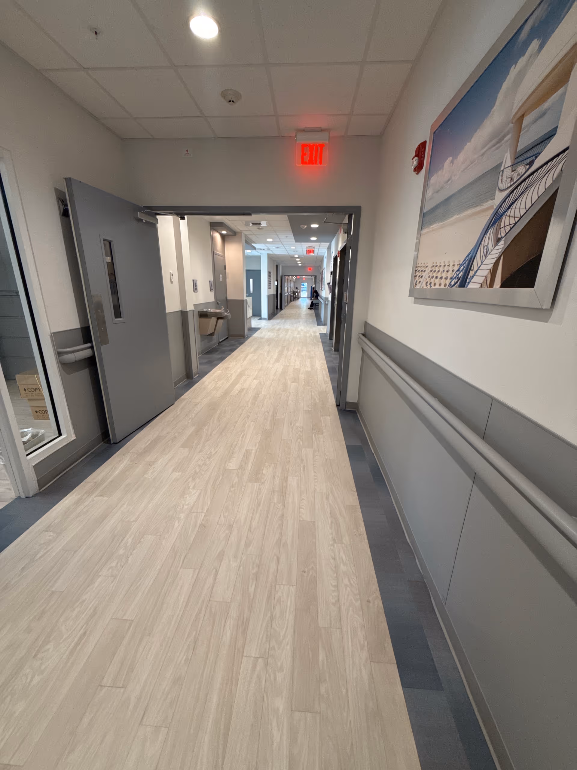 Long well-lit corridor in a senior living facility with doors and wall art.