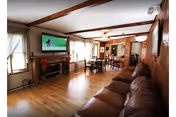 Cozy living area with leather sofa, dining table, TV, and wood beam ceilings.