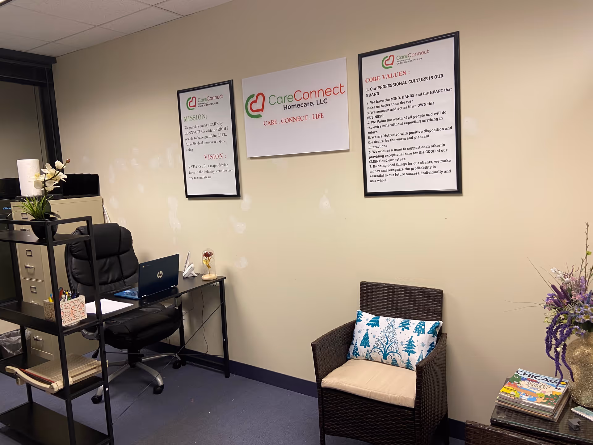 Office area with desk, laptop, wall signs, and a wicker chair in view.