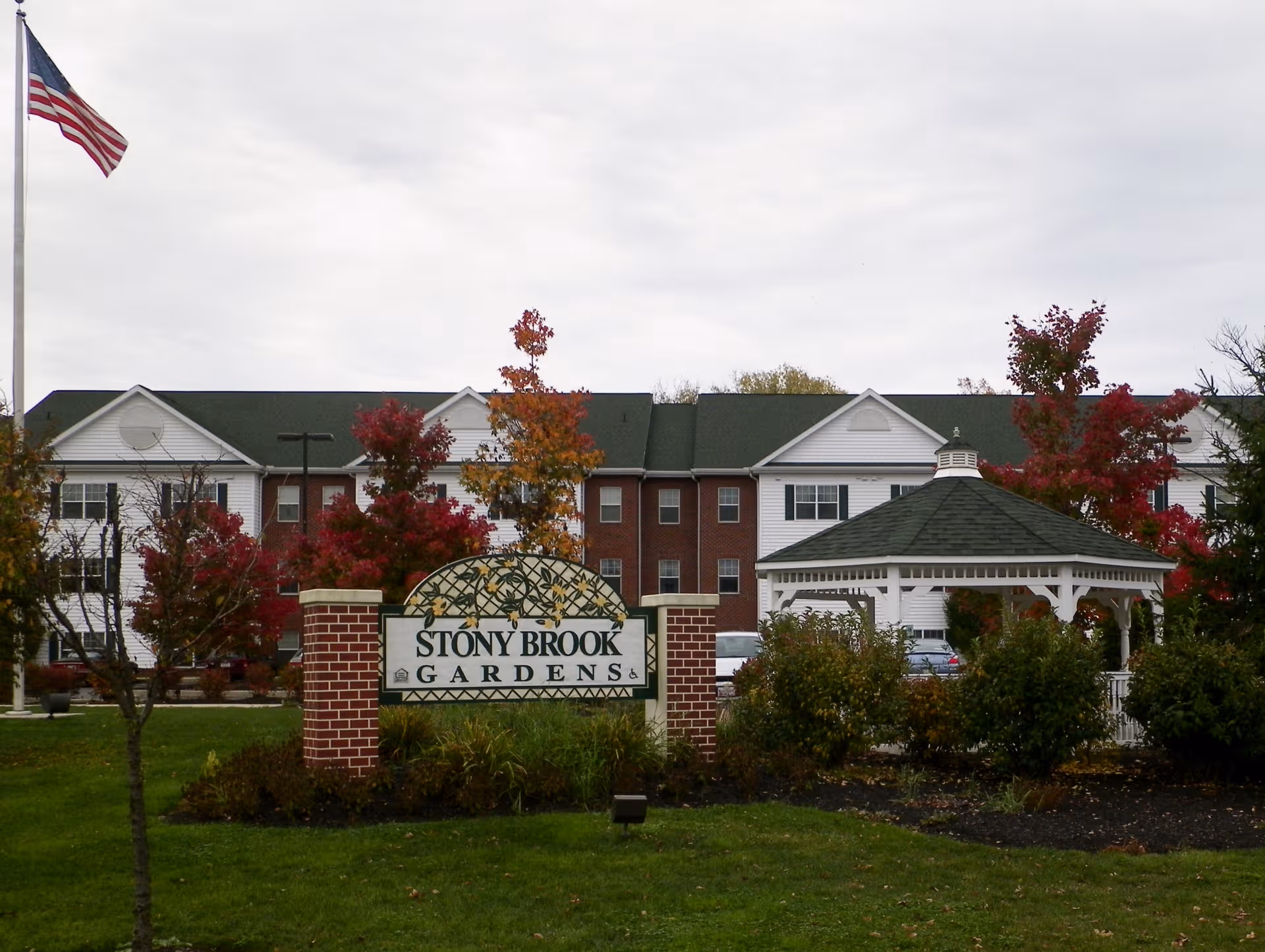 Exterior view of Stony Brook Gardens with the sign, gazebo, flag, and autumn trees.