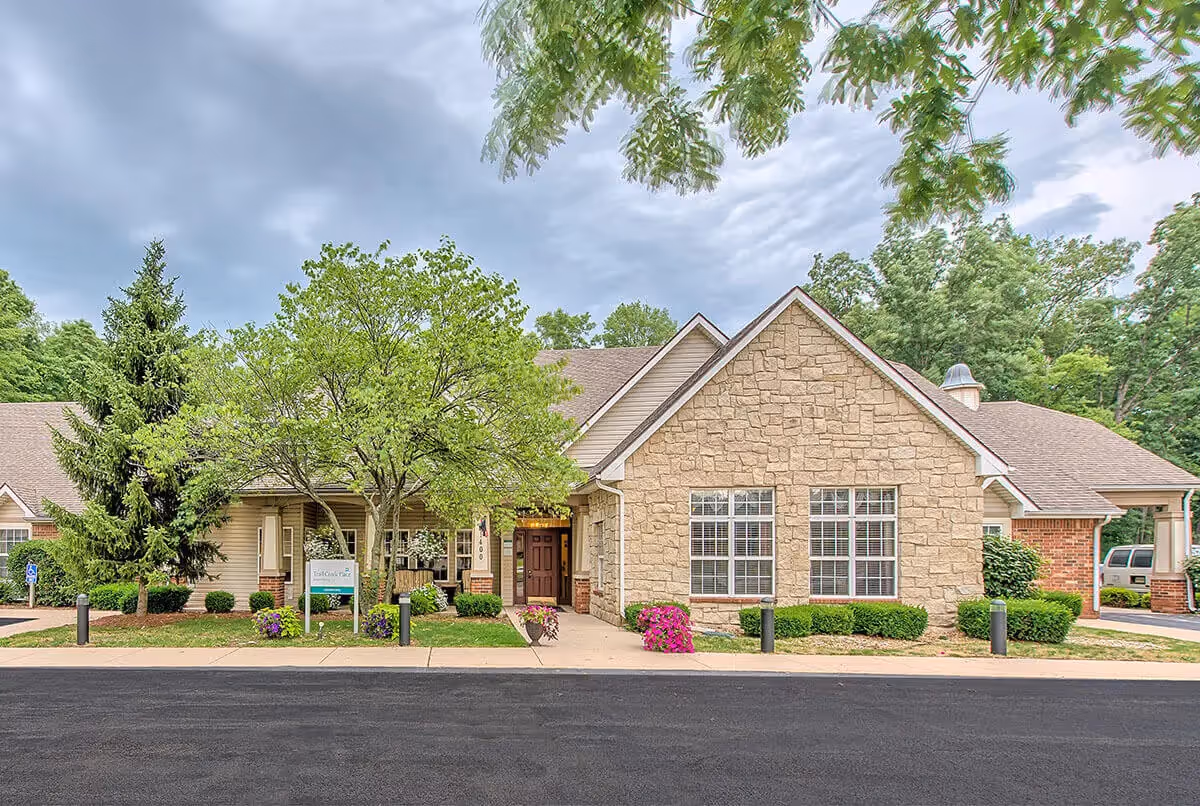 Single-story assisted living building with a stone facade, front entrance, trees and neatly landscaped shrubs.