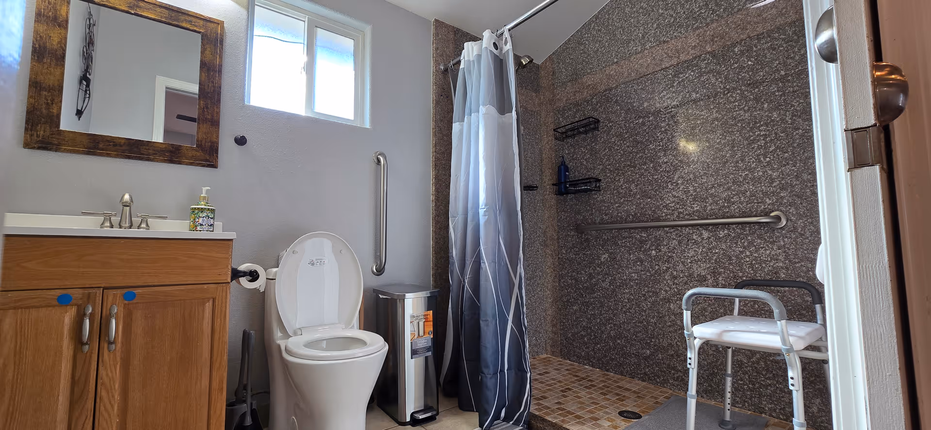 Accessible bathroom in a senior facility featuring a toilet, sink, shower with chair and grab bars.