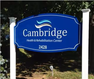 Blue Cambridge Health and Rehabilitation Center sign on white posts outside facility.