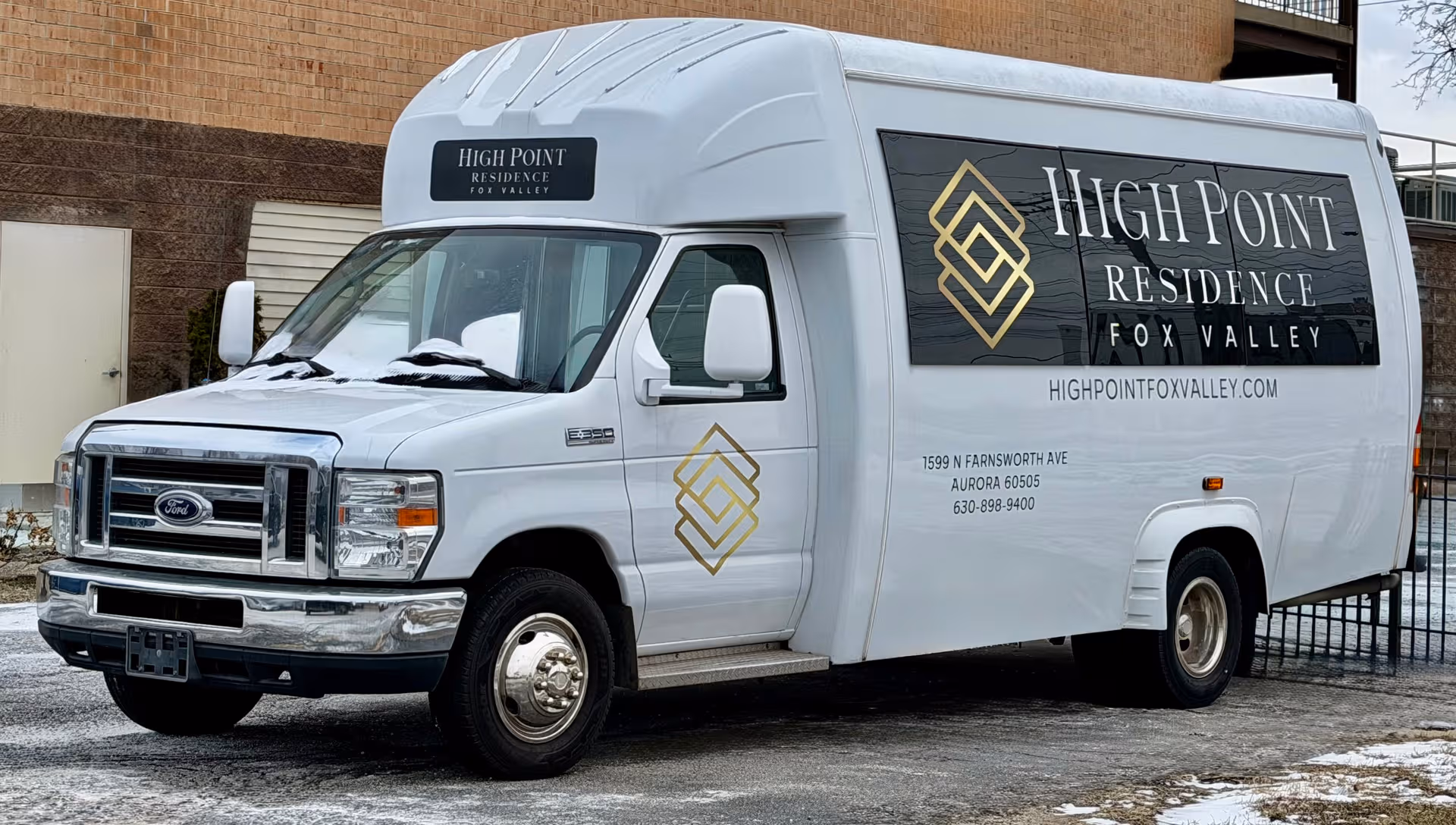 White branded shuttle van parked outside a brick building advertising High Point Residence Fox Valley.