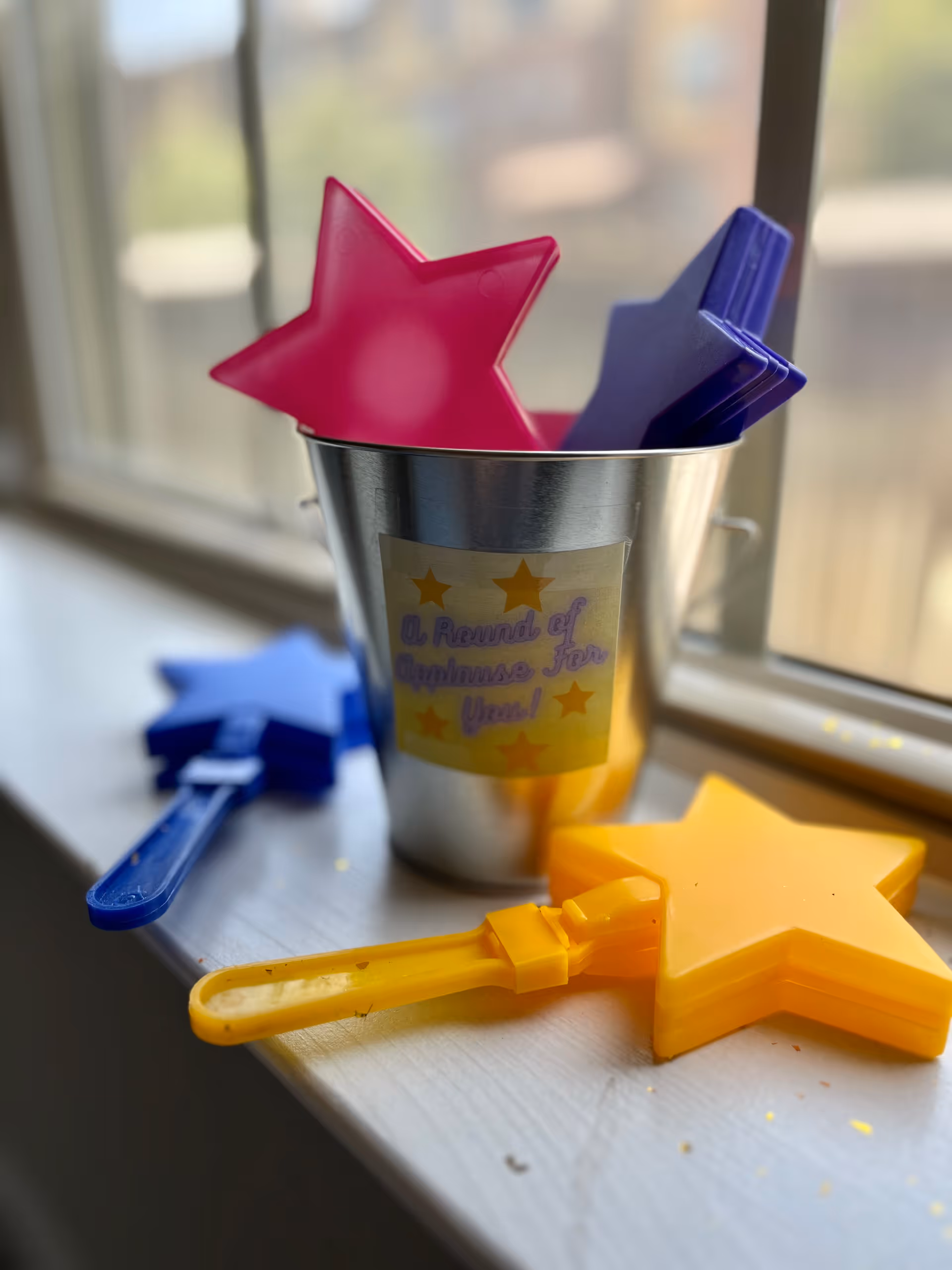 Metal cup holds star-shaped plastic utensils on a bright windowsill, with a reward for kindness label.