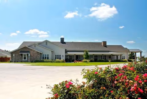 Front view of a single-story senior living facility with lawn and blooming bushes.