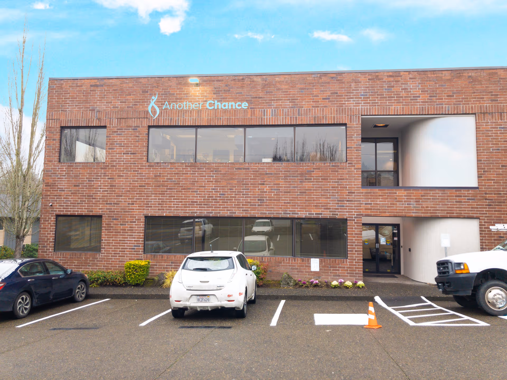 Brick two-story building with large windows and a parking lot in front.