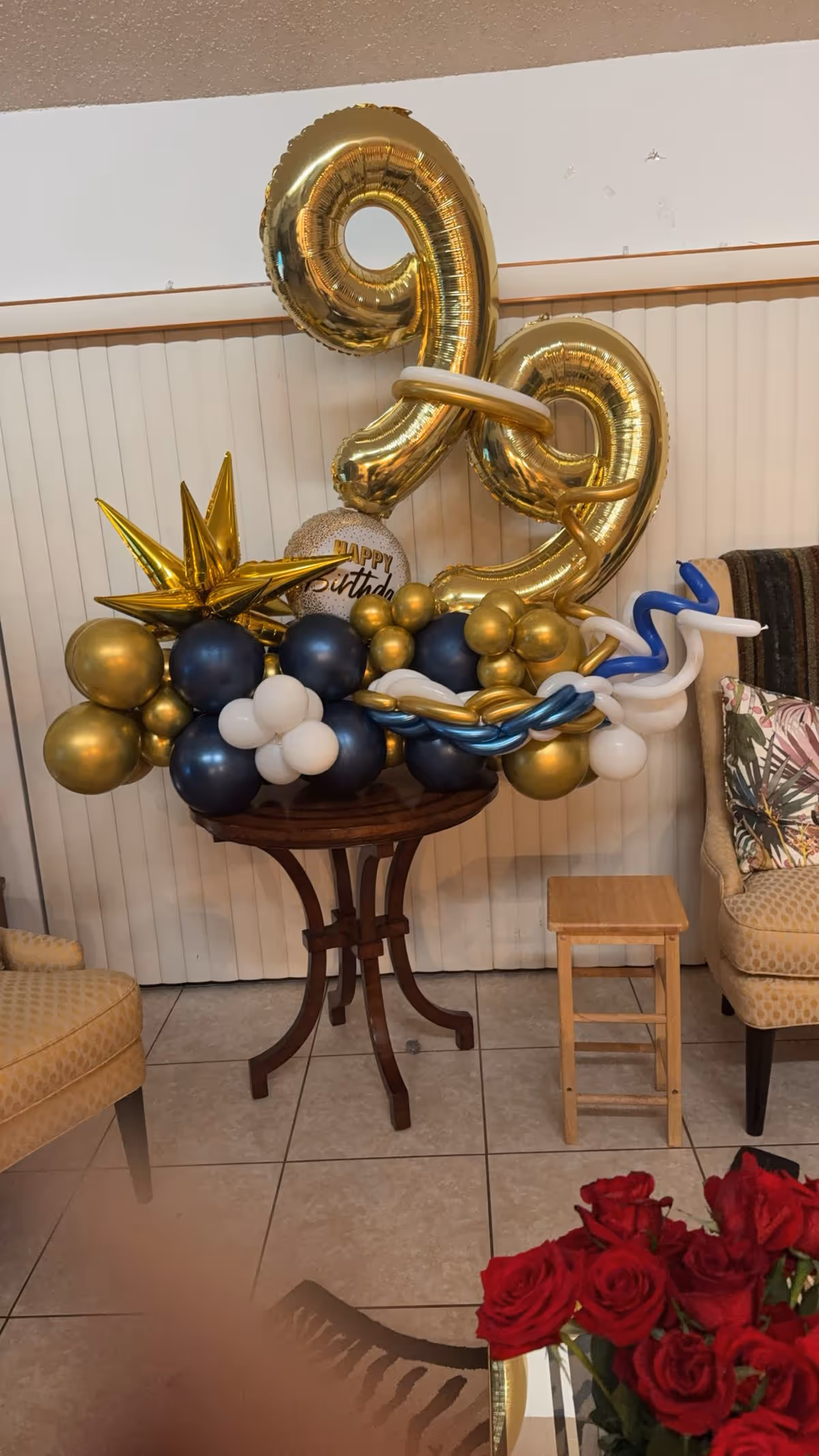 Indoor common area decorated with gold and blue birthday balloons around a pedestal table.