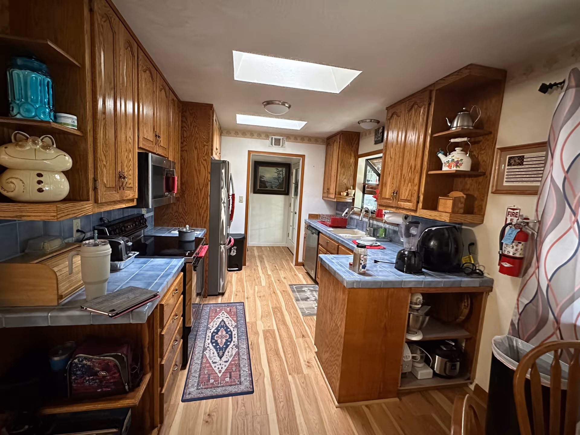 Long kitchen with wooden cabinets, skylights, and assorted appliances.