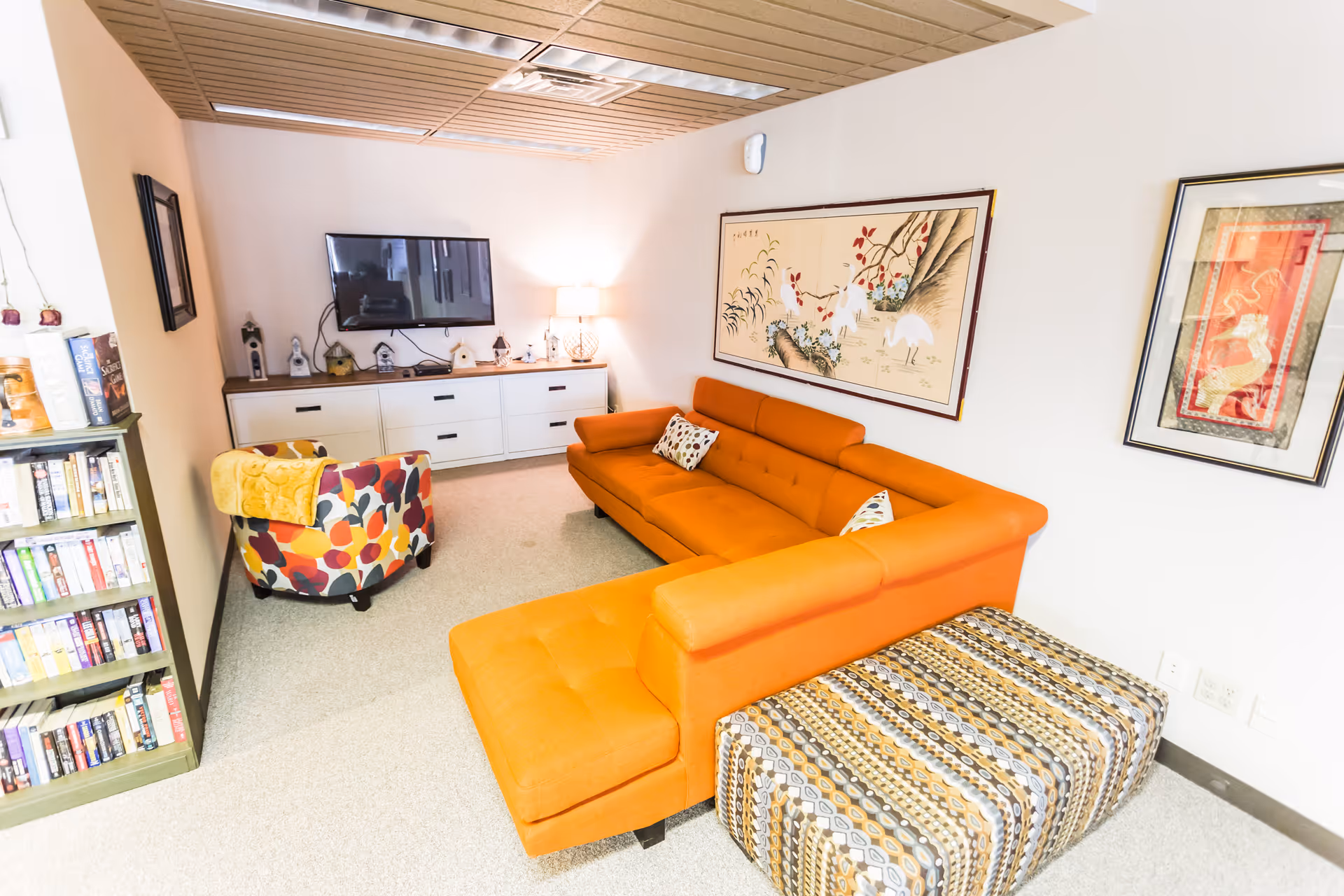 Orange sectional sofa, patterned ottoman, and wall art in a cozy living room.