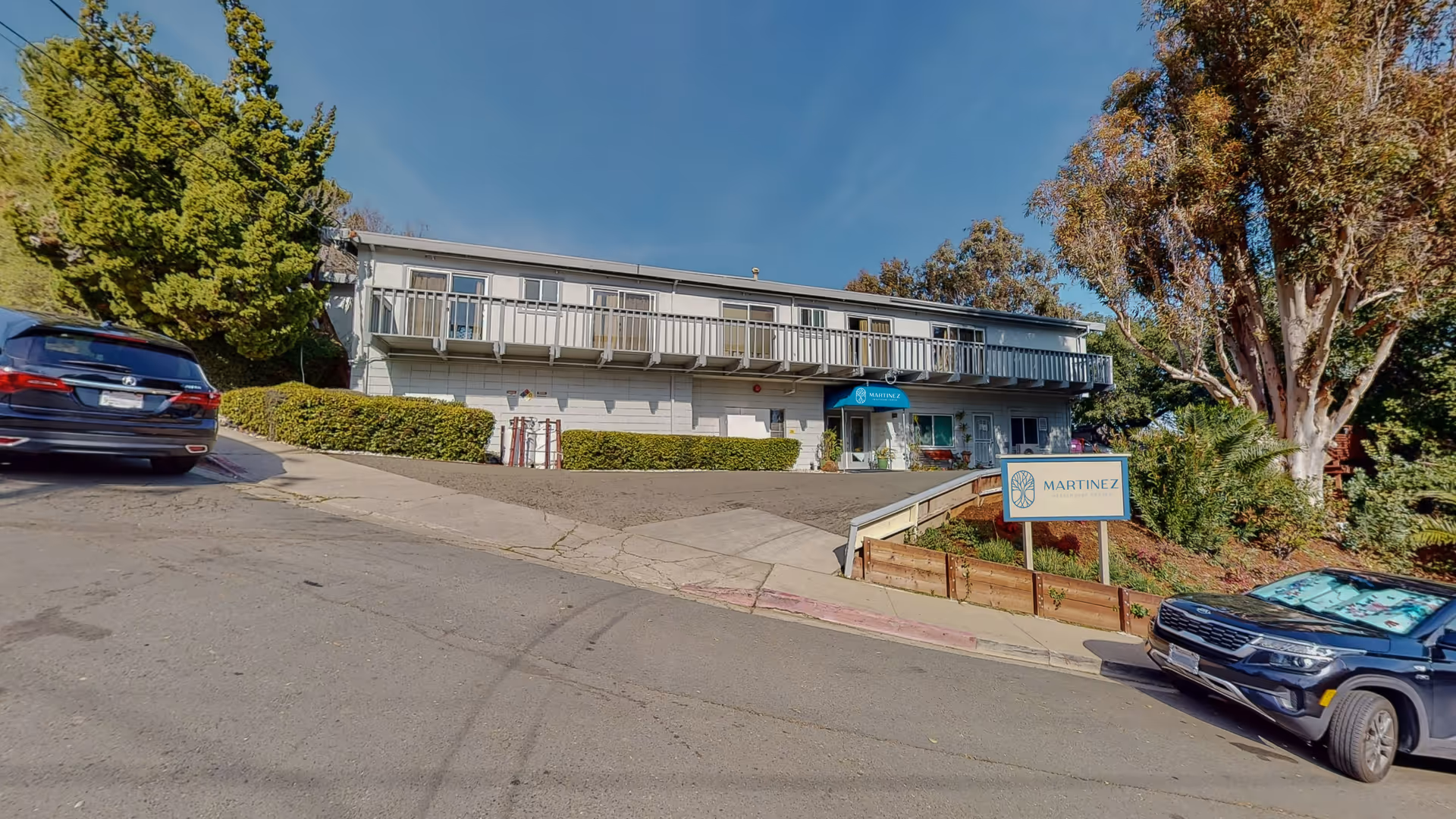 Exterior view of a two-story senior living facility with Martinez sign, parked cars, and landscaping.