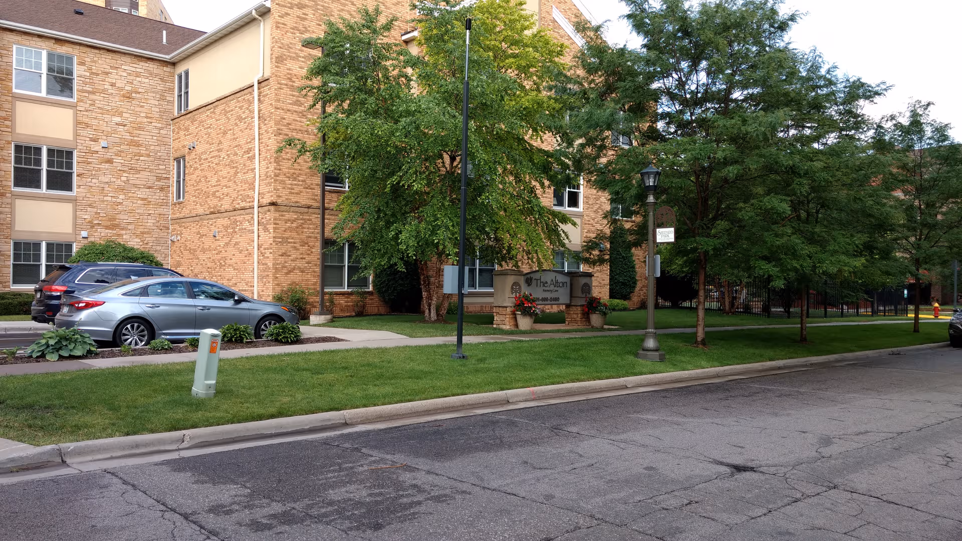 Brick senior living building exterior with cars, trees, and a landscaped entrance sign.