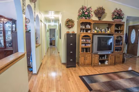 A warm, wood-floored hallway in Elisabeta's Loving Care leads to a living room with a TV.
