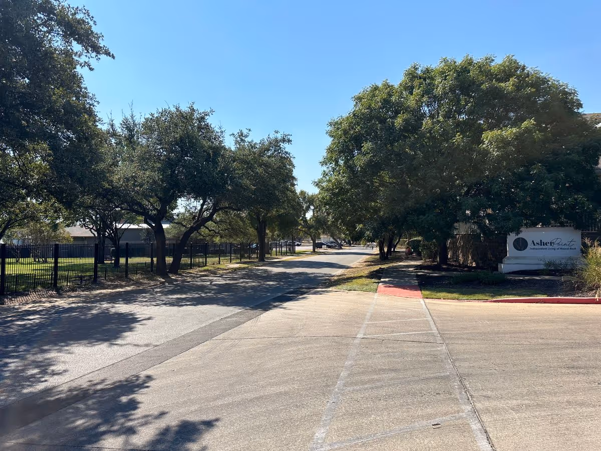 Driveway and tree-lined entrance to Asher Point Independent Living of Round Rock with the facility sign visible on the right.