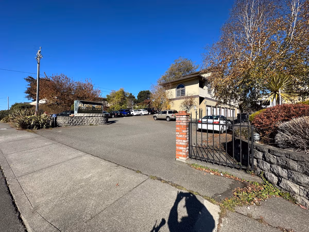 Exterior view of Alder Bay Assisted Living facility with entrance gate and parked cars.