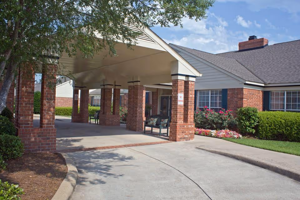 Exterior view of a covered brick entrance with benches and landscaping.