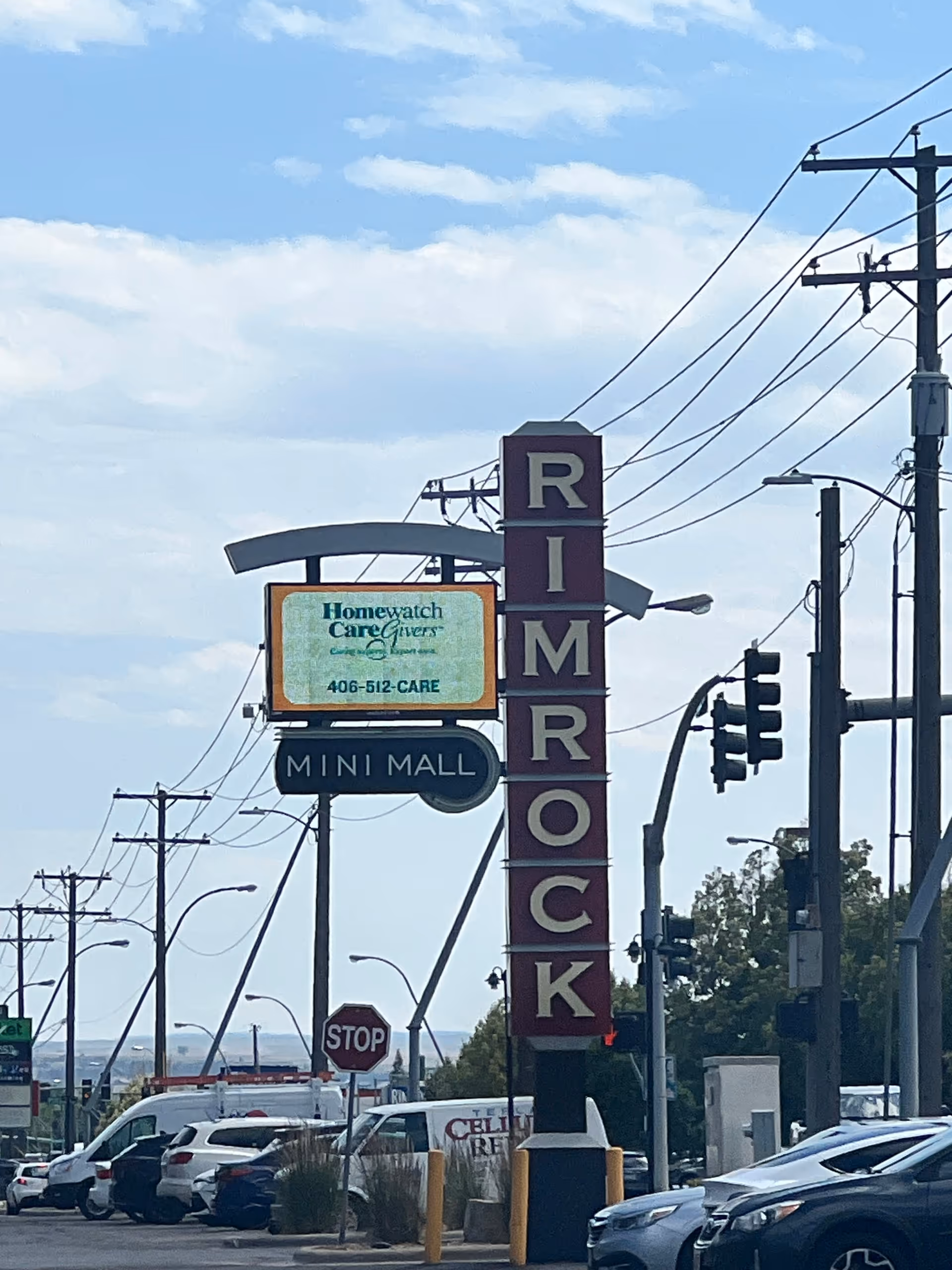 Street view with a Homewatch CareGivers sign and a tall Rimrock sign beside parked cars.