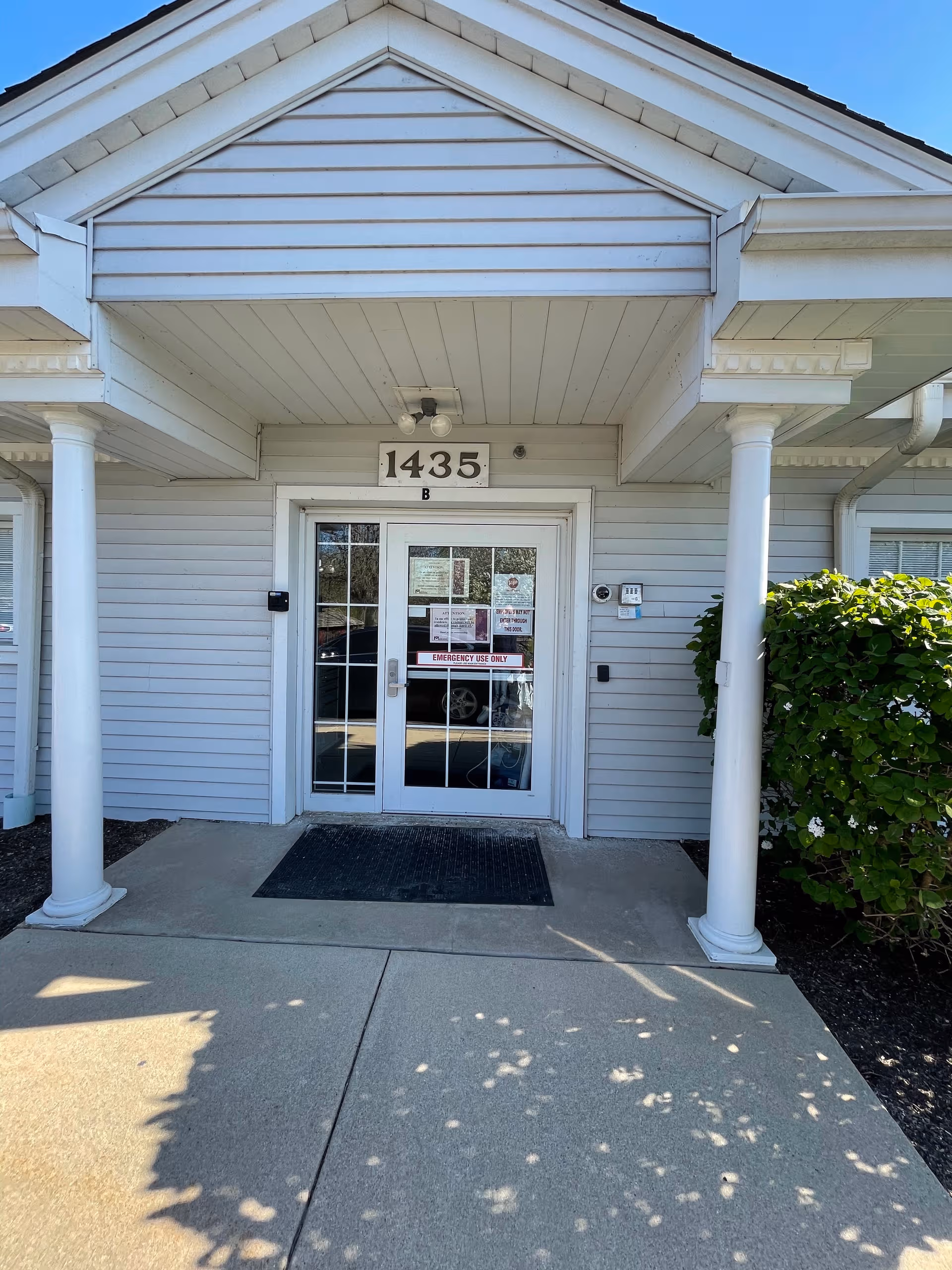 White entrance with double doors, pillars, and address plaque at the front of a senior facility.