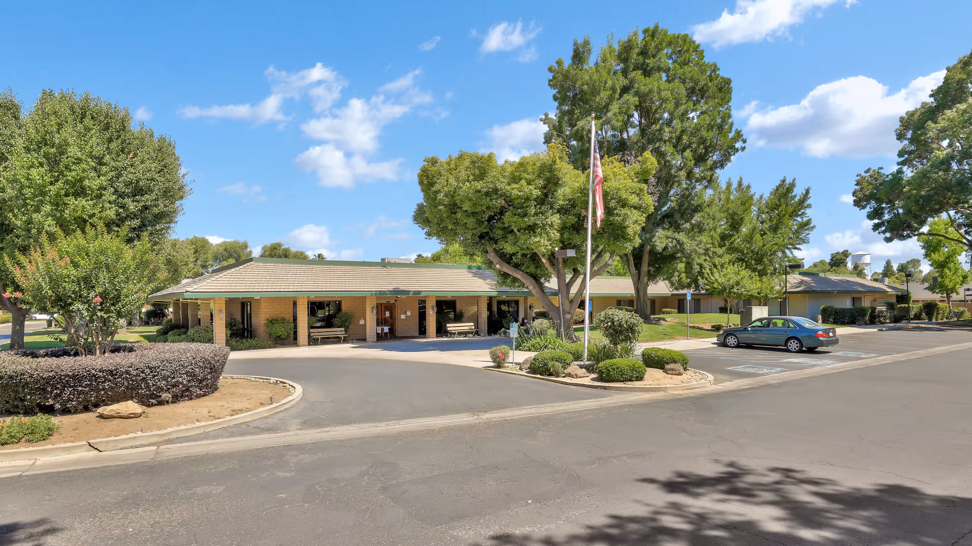 Front exterior view of a single-story senior living facility with a circular driveway and trees.