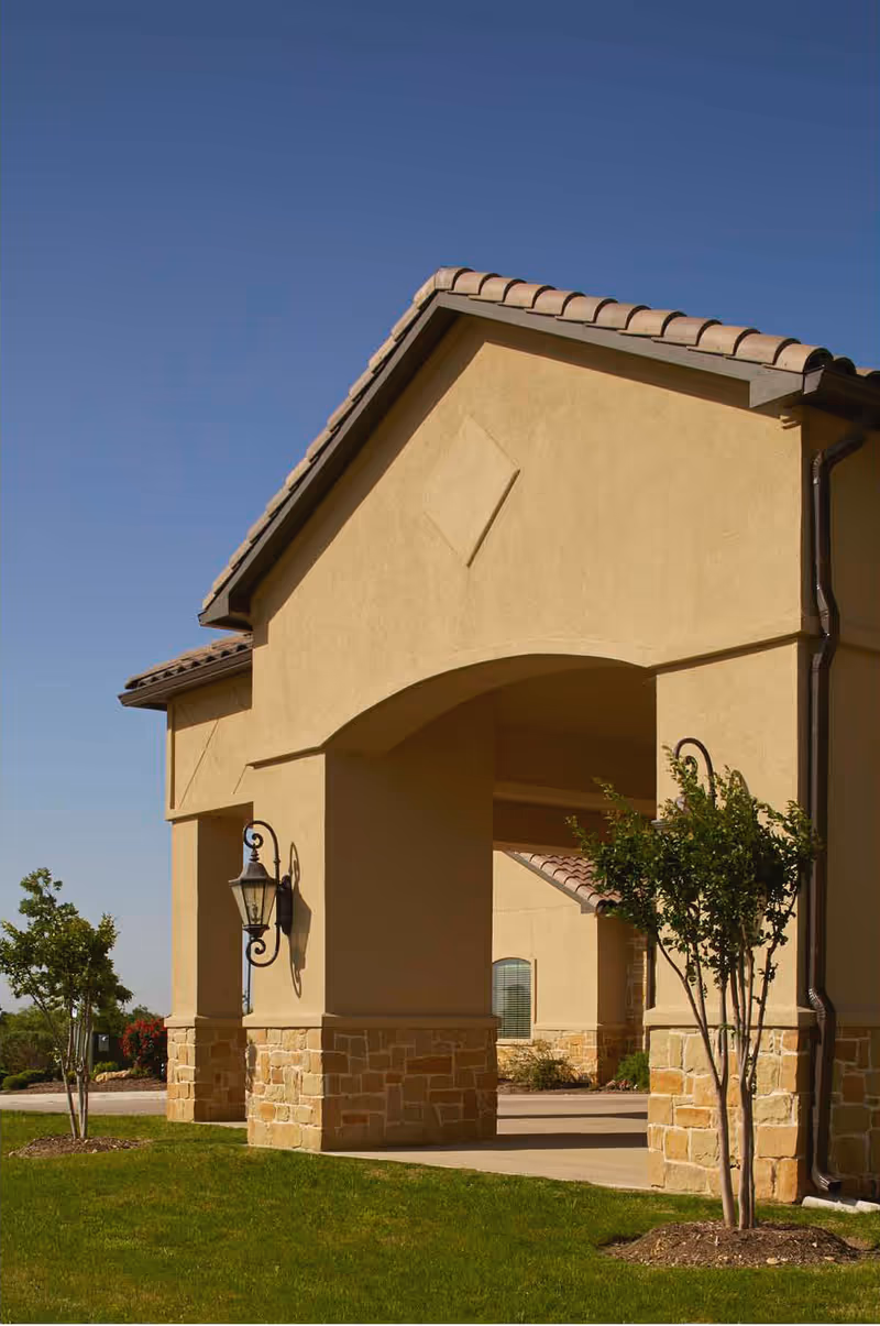Exterior view of a beige senior living facility entrance with arches.