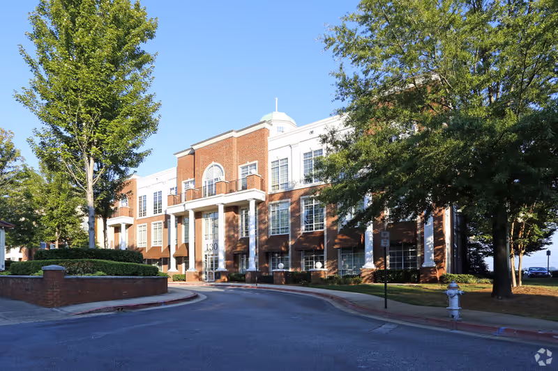 Brick senior living building with columns, trees, and a curved entry road.