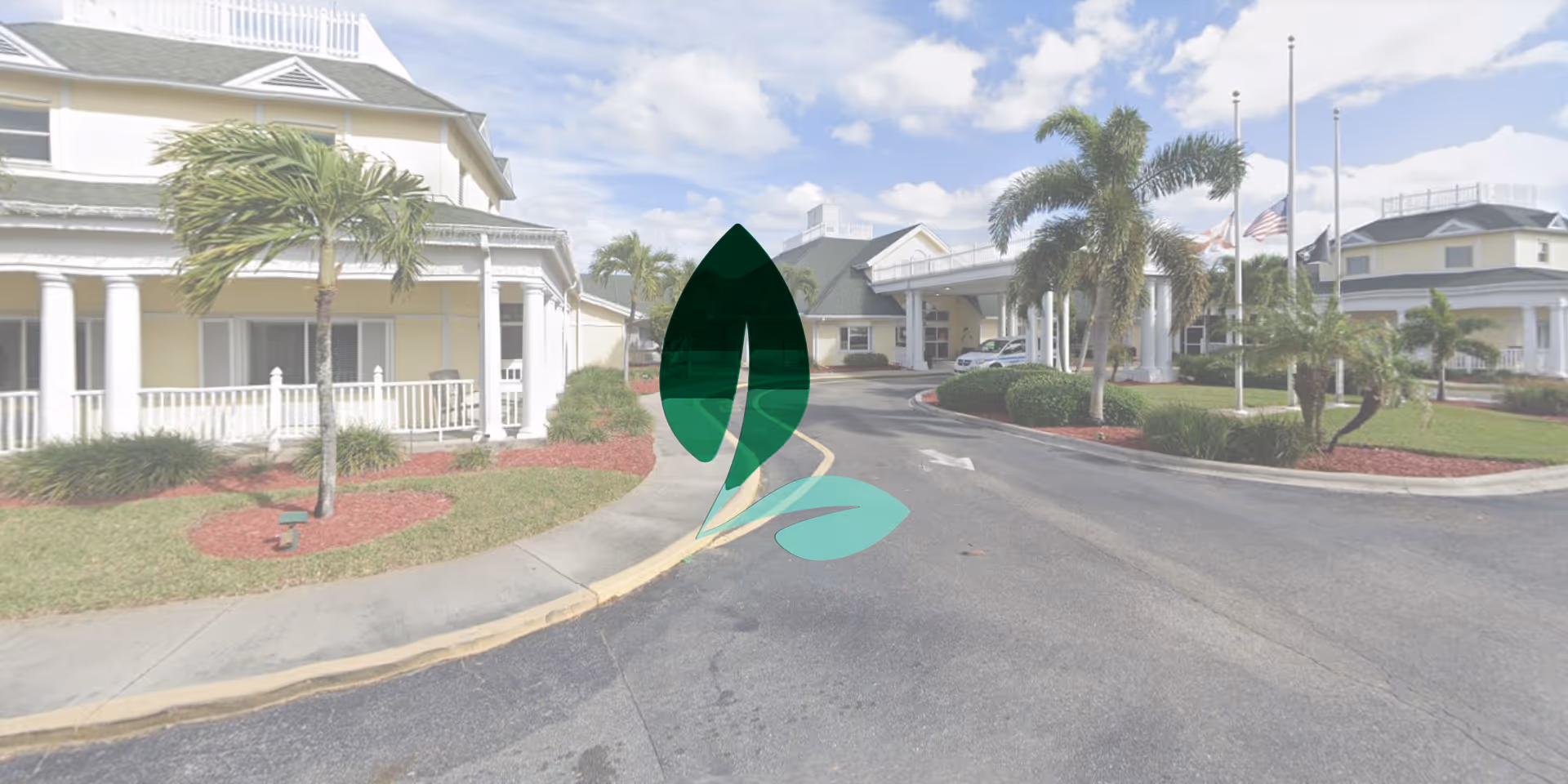 Exterior view of Page Rehabilitation and Healthcare Center showing a driveway entrance with landscaped areas including palm trees and bushes. The building features a light yellow facade with white columns and a covered entrance. The sky is partly cloudy.
