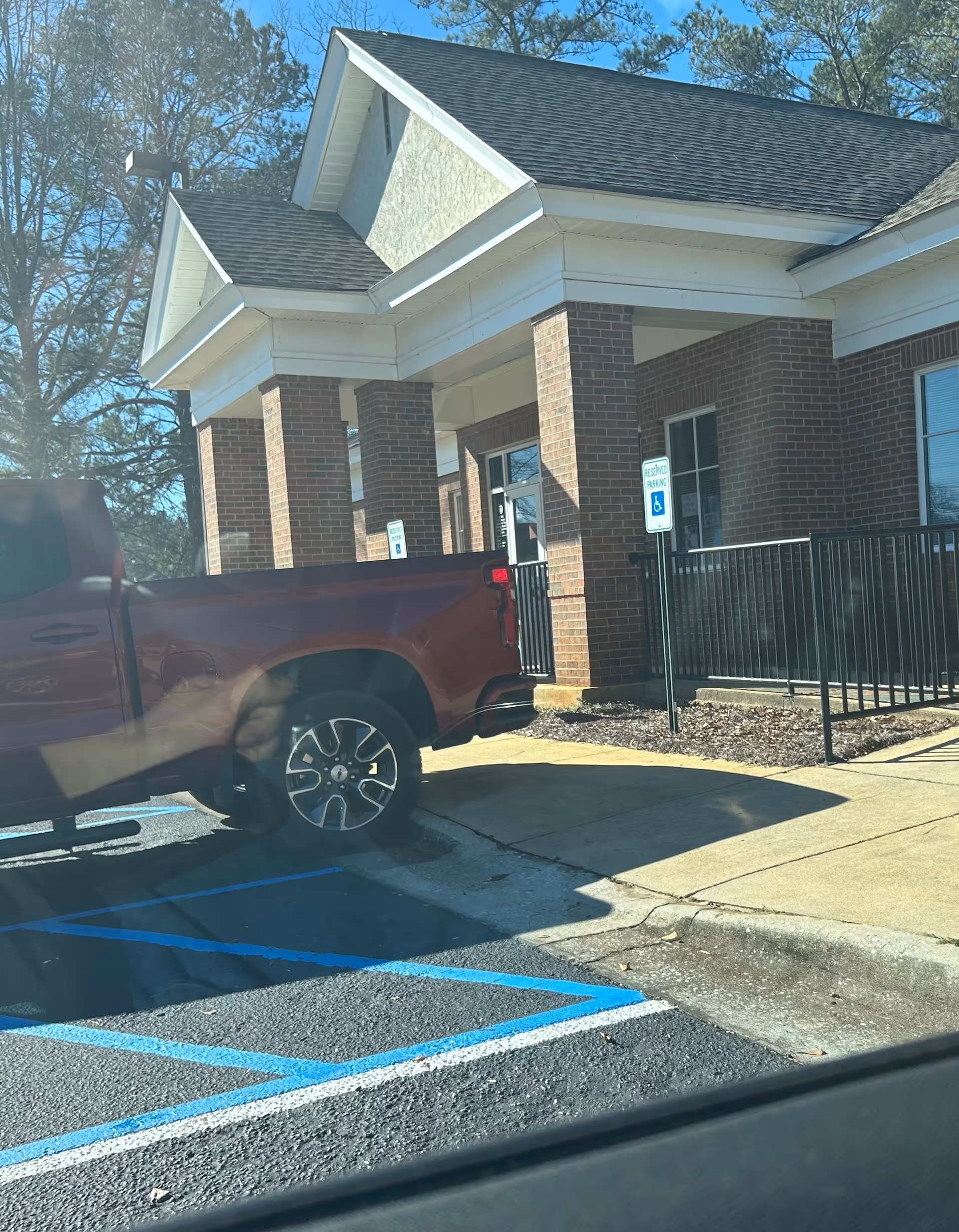 Brick-front health department building entrance with wheelchair sign and a parked pickup in a handicapped space.