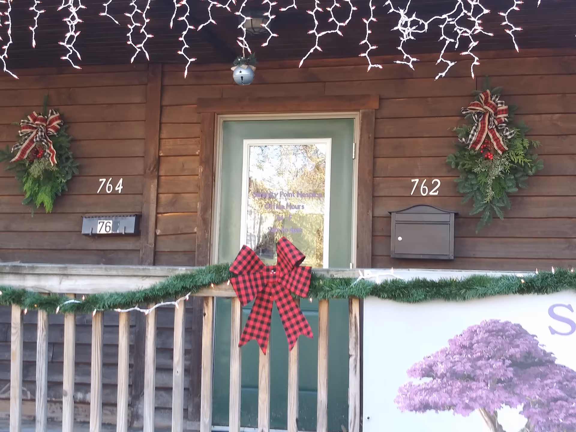 Wooden building exterior with holiday wreaths, garland, and a green front door.