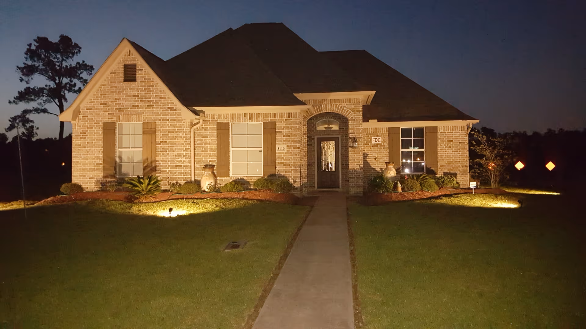 Nighttime view of a brick senior living facility's front entrance with landscaped yard.