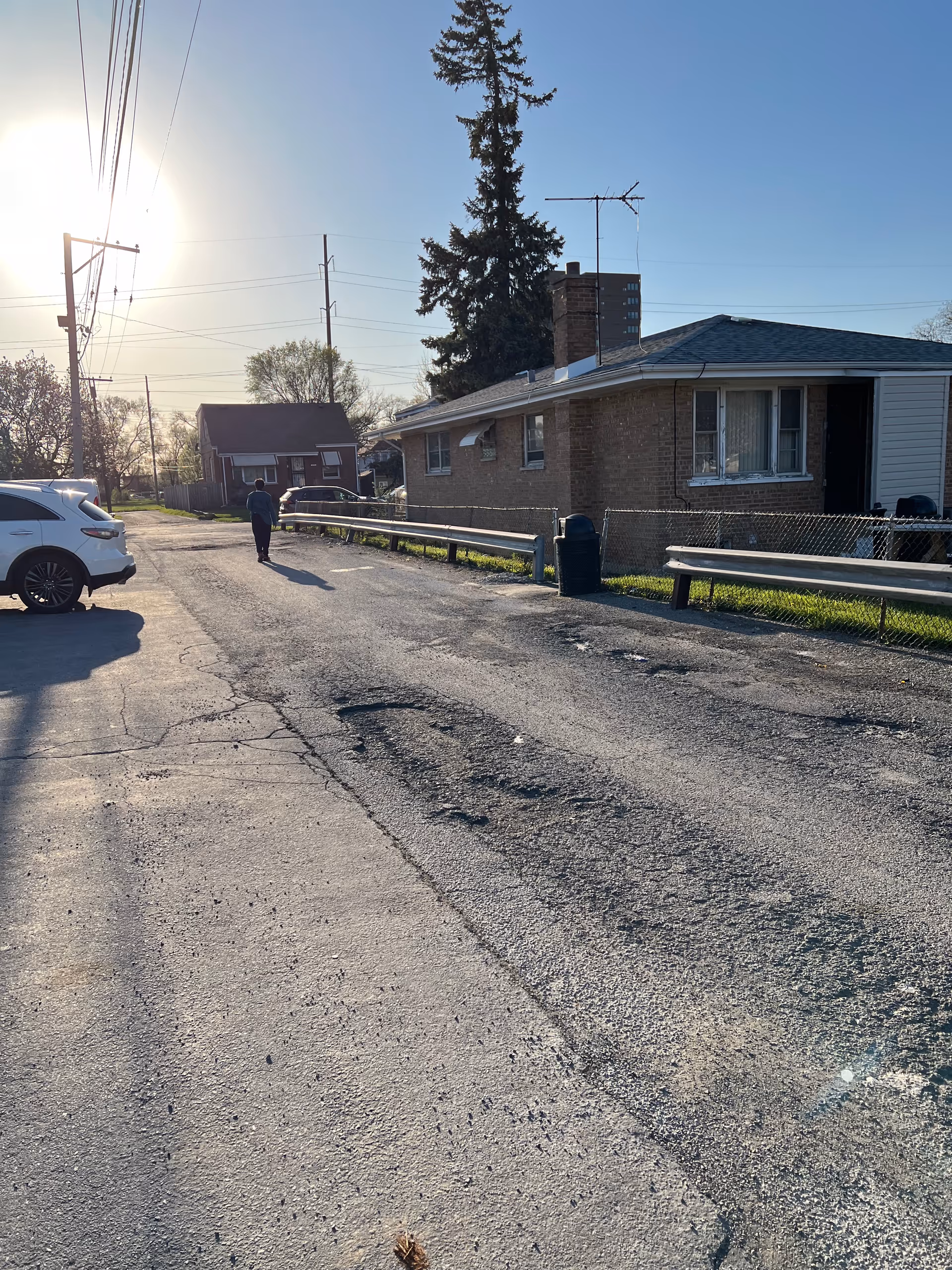 A quiet residential street with a brick single-story building, parked car, and a person walking away.