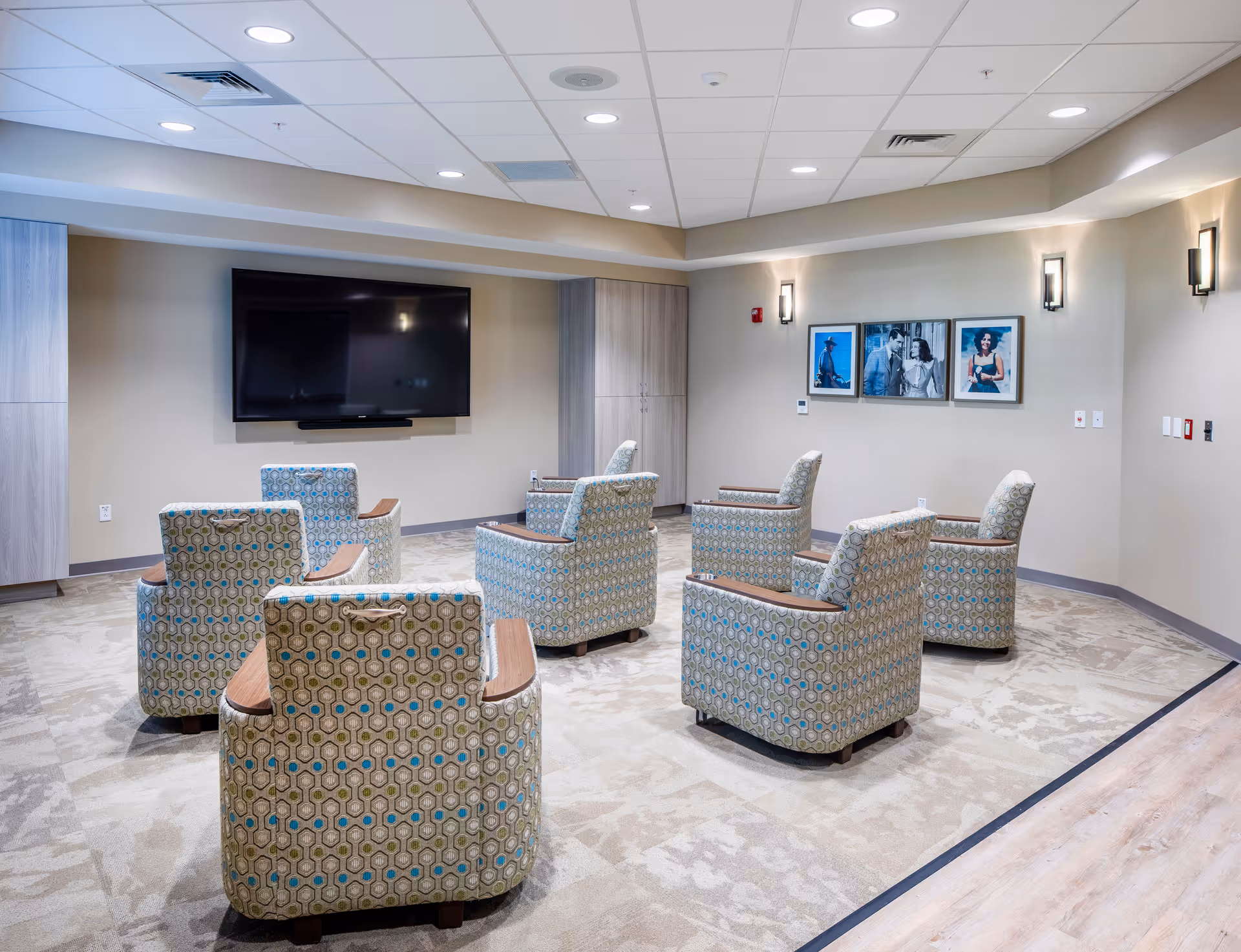 Spacious resident lounge with patterned chairs arranged around a wall-mounted television.