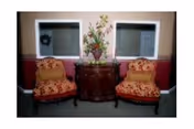 Two ornate red-upholstered armchairs flank a wooden console table with a vase against a beige wall.