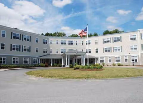 Front view of The Residence at Great Woods, a light-colored residential building with a circular driveway.