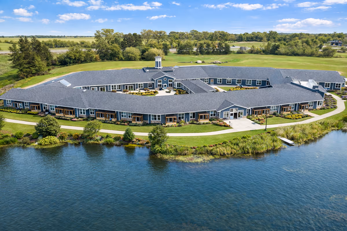 An expansive, single-story Bella Largo Senior Living campus with a blue roof sits along a lake.