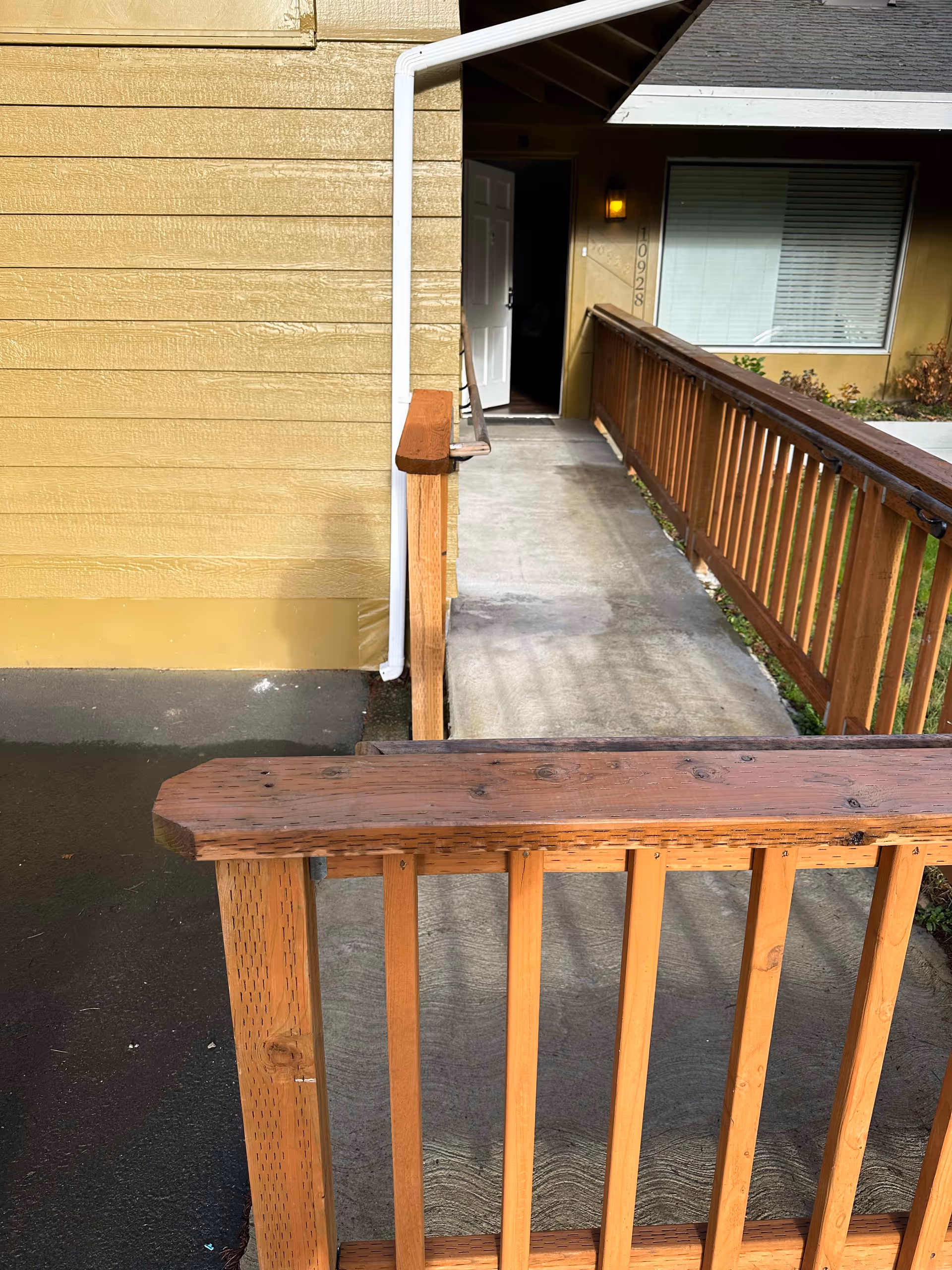 Wooden ramp and railing leading to a yellow building entrance with an open door.